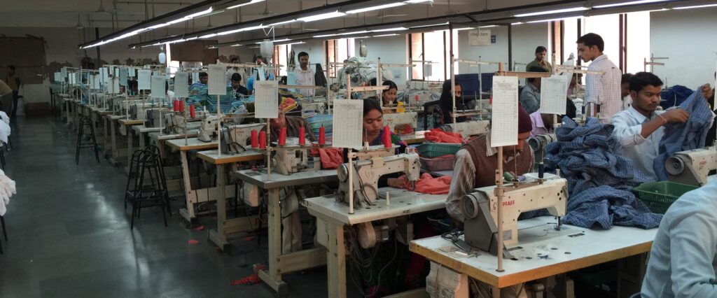 A busy garment factory with workers sewing and inspecting clothing, representing Fair Trade Certified manufacturing that upholds ethical labor practices and ensures safe working conditions.